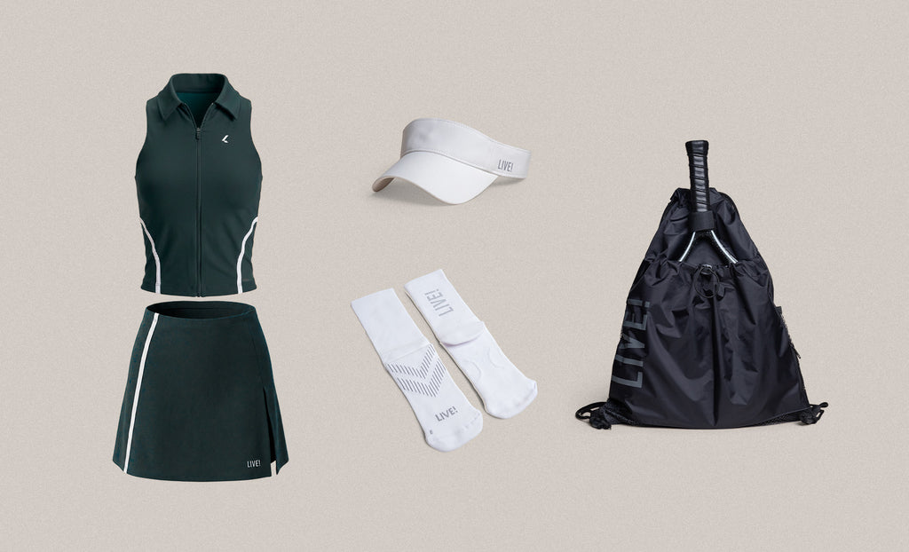 A coordinated athletic outfit and accessories set on a plain beige background: a dark green sleeveless zip-front top, matching dark green skirt with white side stripes, a white visor, a pair of white crew socks, and a black drawstring bag with a tennis racket resting inside.